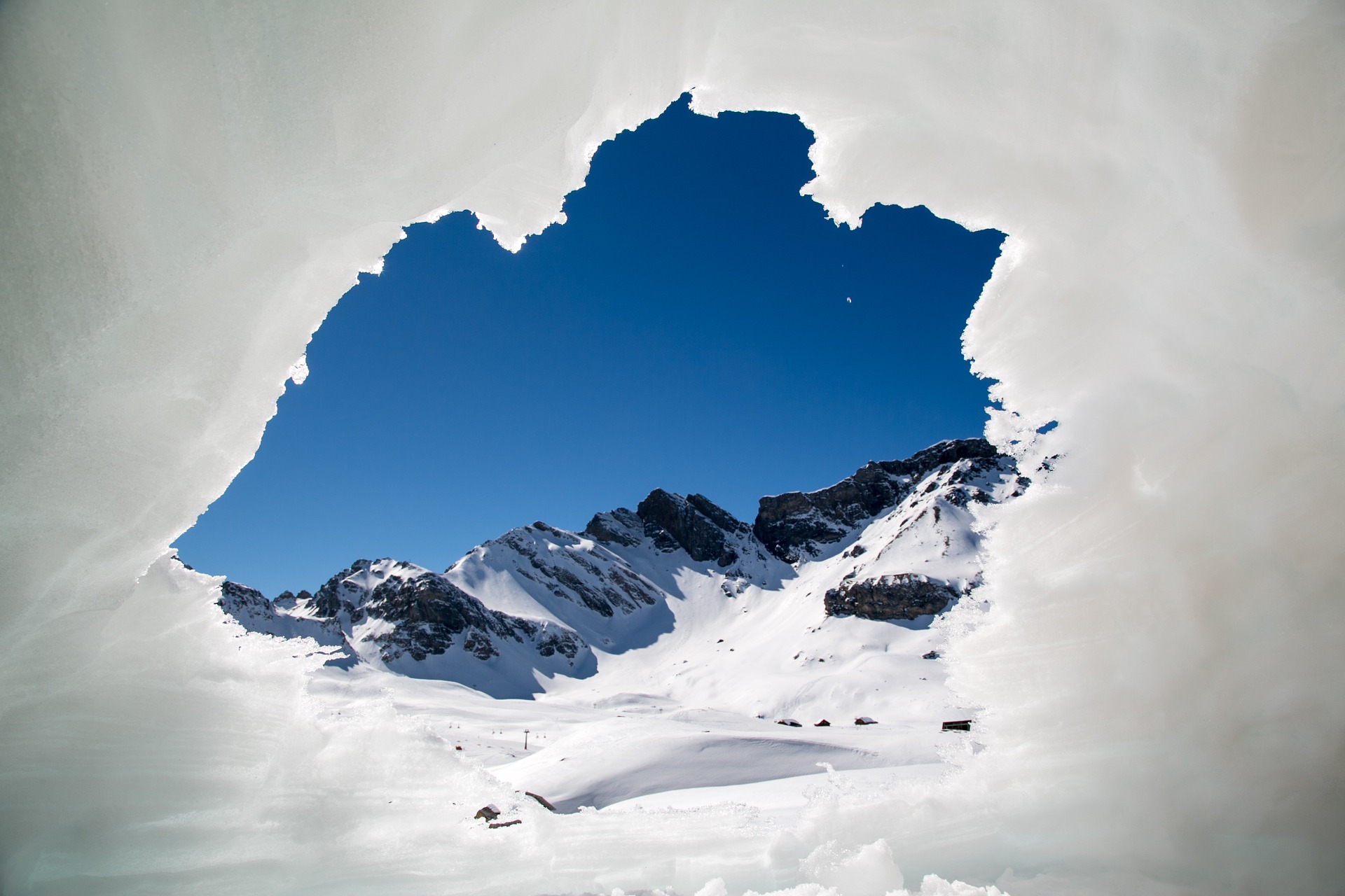 looking out a snow cave to the snow covered mountains and blue sky