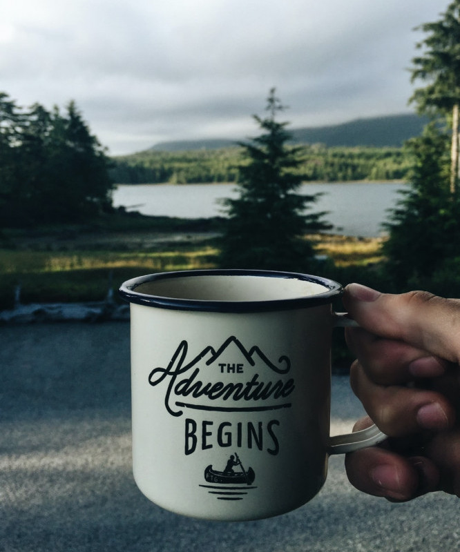 A mug with forest in the background, the mug says, "The Adventure Begins"