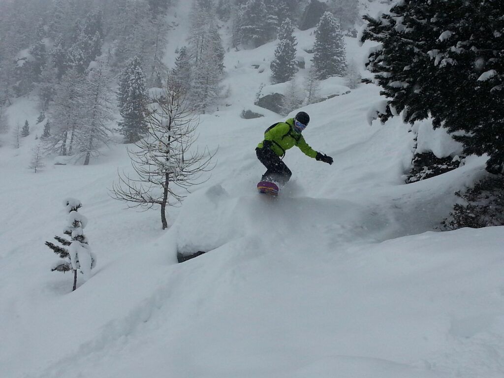 snowboarder going downhill through fresh powder and trees